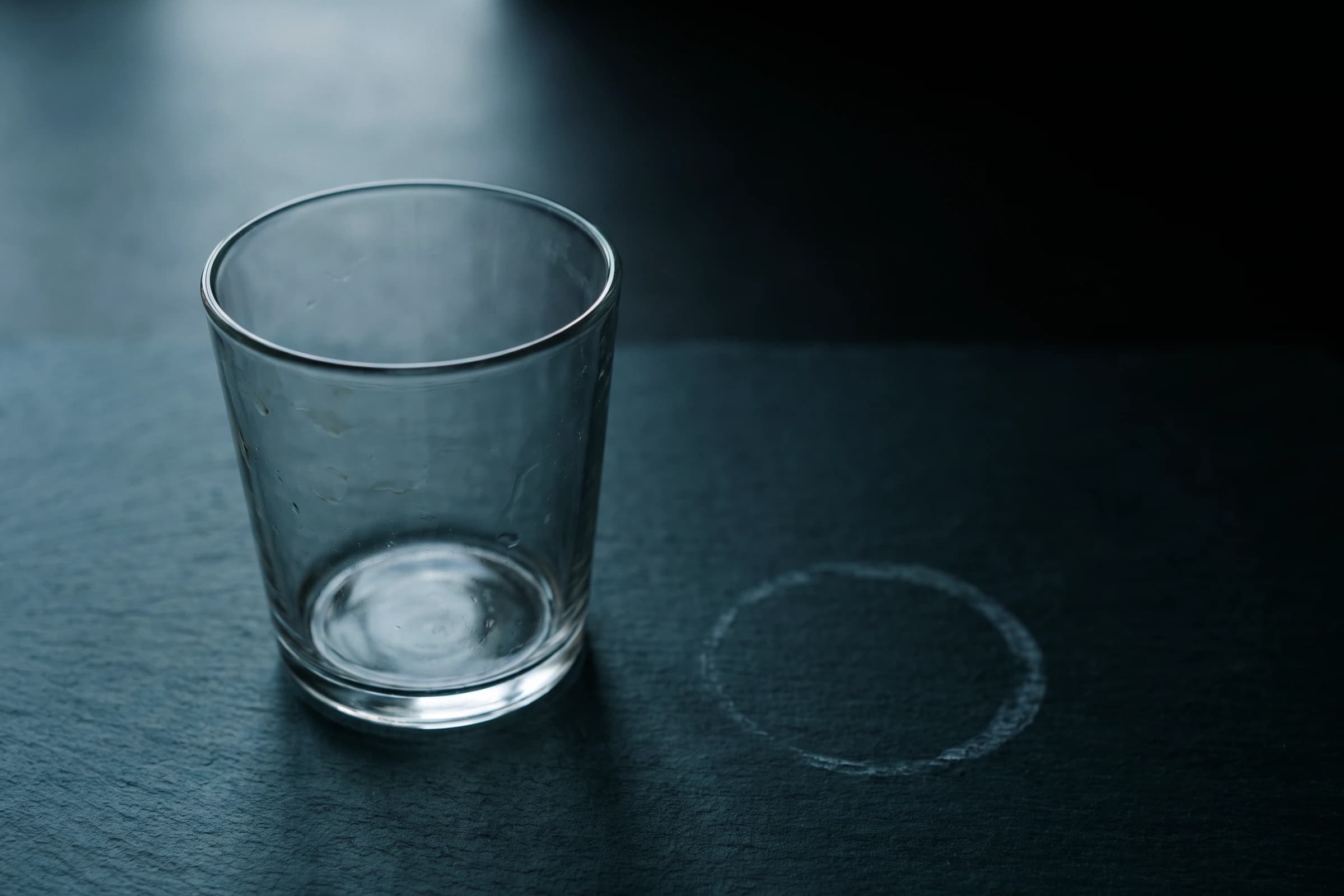 Ein leeres Trinkglas, daneben der eingetrocknete Ring eines früheren Glases
