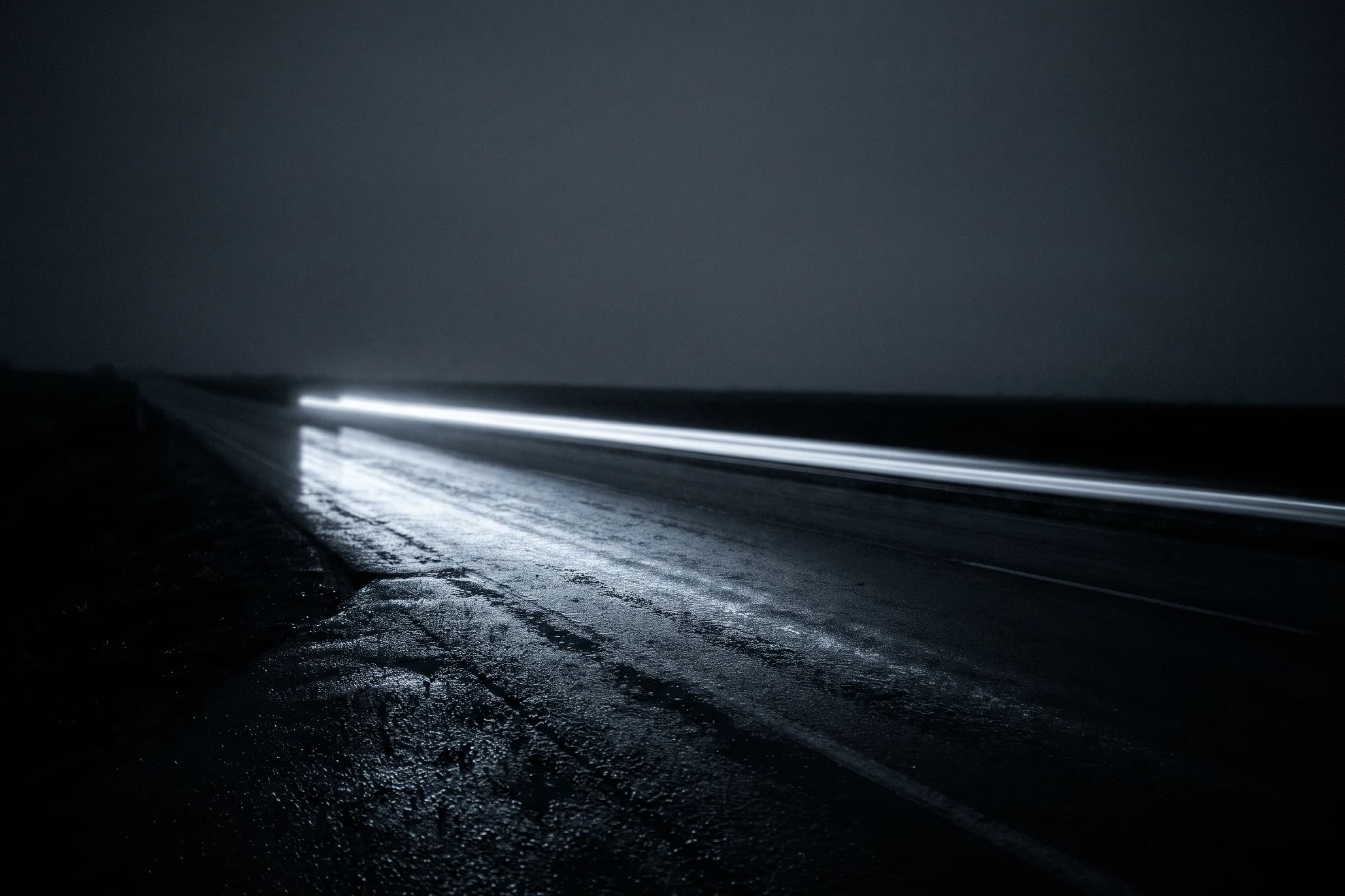 Eine nasse Fahrbahn bei Nacht, angeschnitten von einer einzelnen Lichtspur